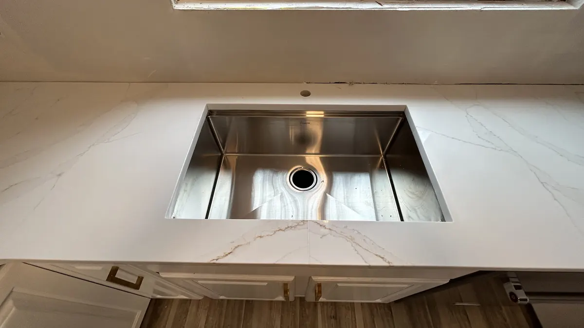 Stainless undermount sink set into a new quartz countertop, ready for the plumber
