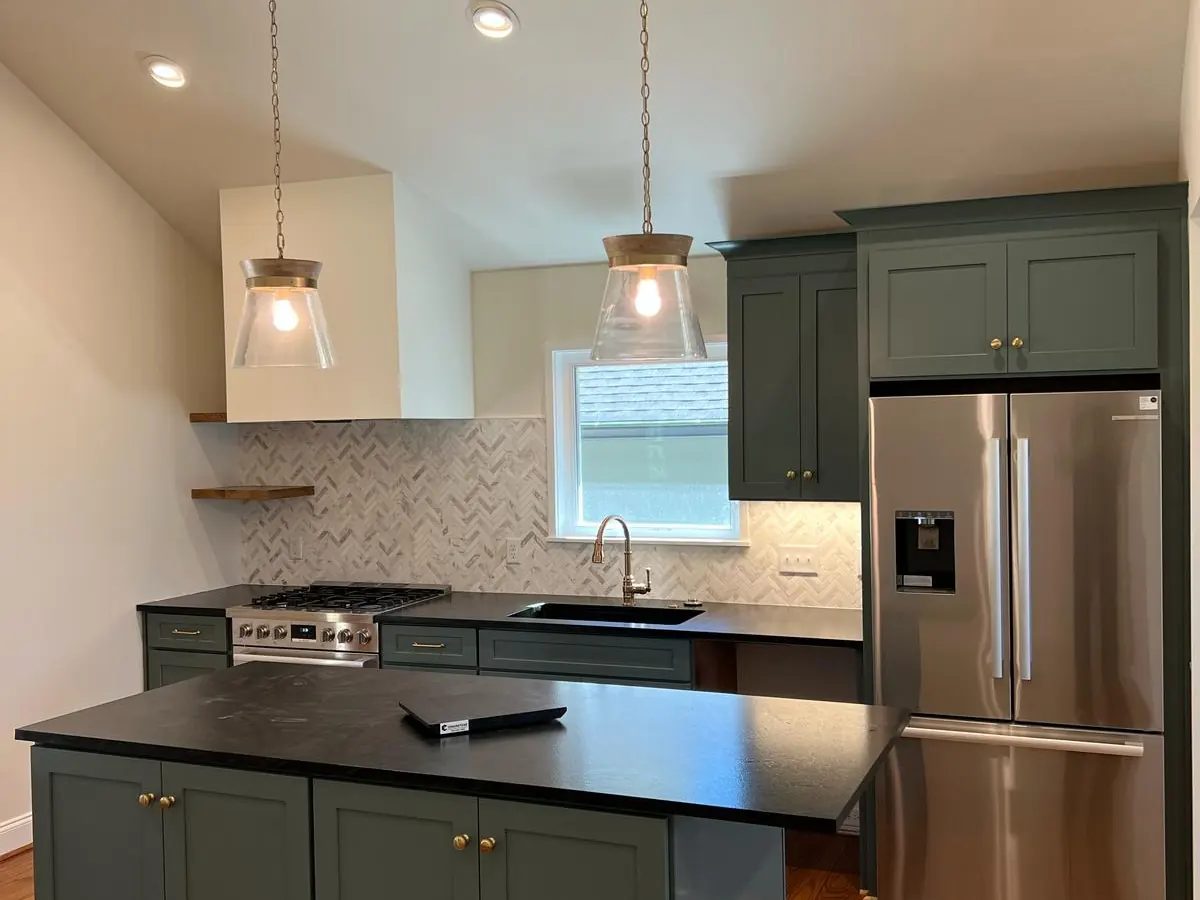 Green kitchen cabinets with a black stone countertop island