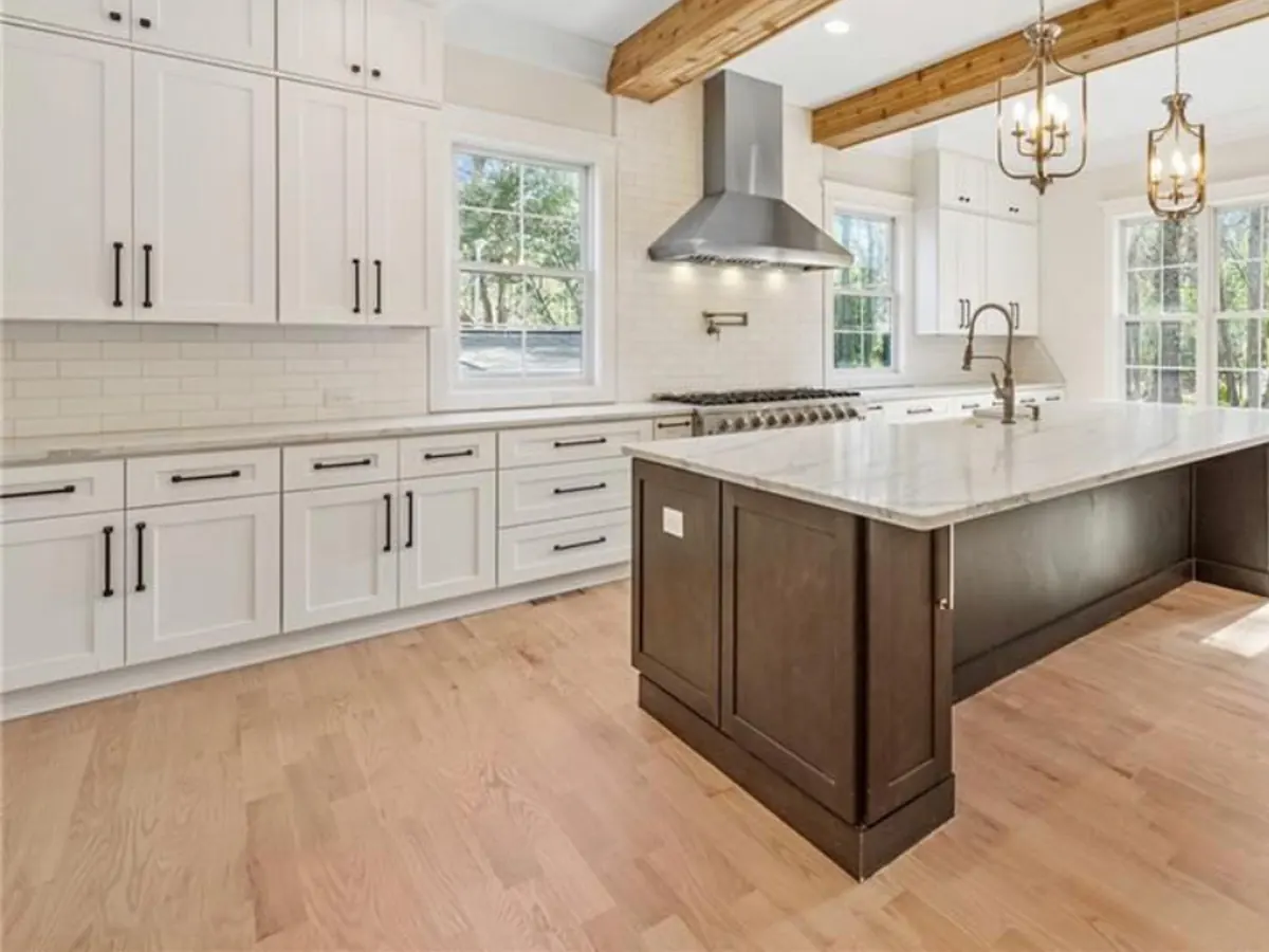 White marble-look kitchen countertops and a dark wood island under cedar ceiling beams