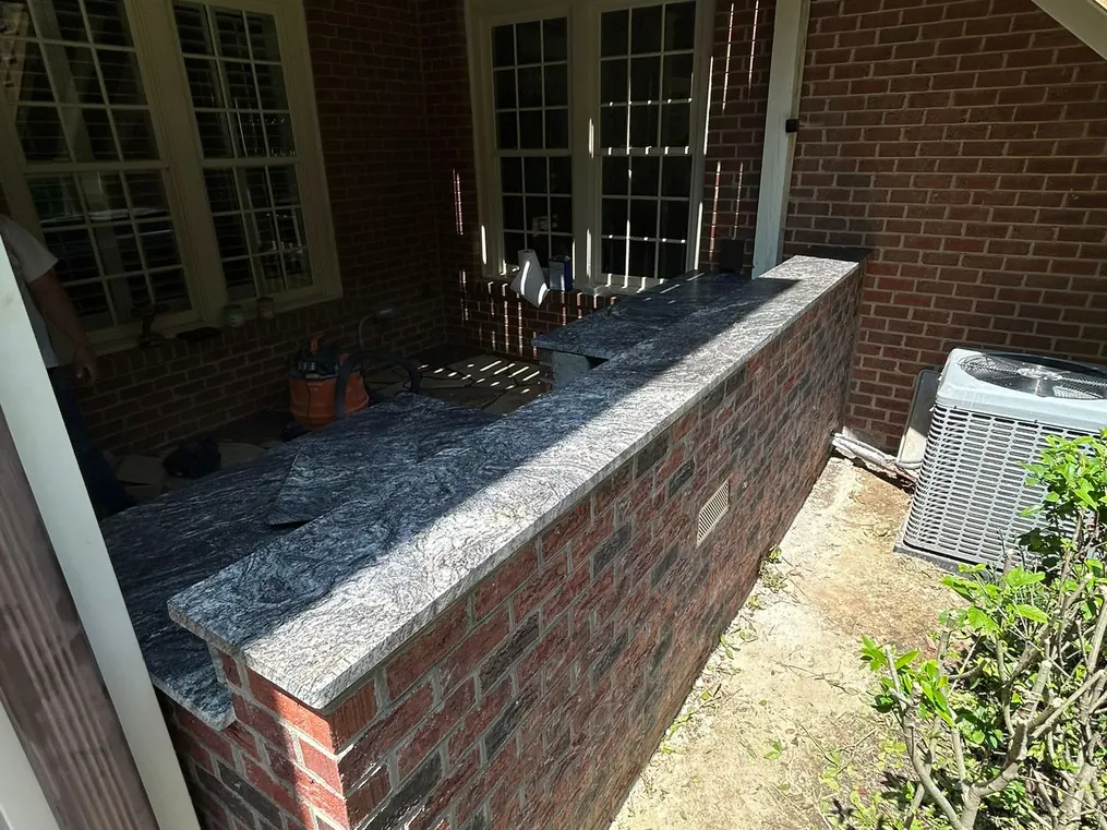 Outdoor kitchen with a granite countertop on a brick grill island