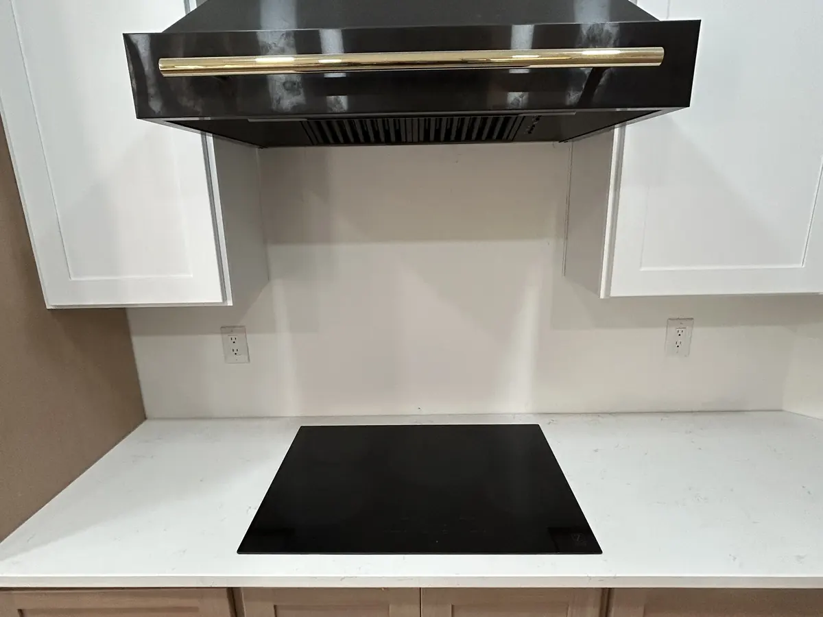 Stone backsplash behind a cooktop and black hood